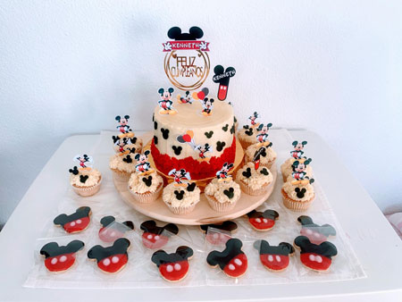 Tarta de Mickey Mouse decorada con detalles personalizados, rodeada de cupcakes y magdalenas a juego. Diseño temático ideal para cumpleaños. 